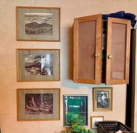 Overall wall showing three framed landscape prints, wooden cupboard, smaller prints and bamboo pole