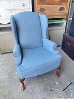 Full front view of blue wingback chair showing upholstery and wooden legs