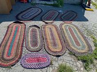 Seven of eight oval braided rugs laid out showing size range and colours