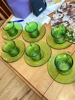 All six green glass teacups with matching saucers displayed on table