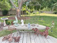 Overall lot laid out on deck showing concrete statues, metal rooster, wind spinner, trellises and ornaments