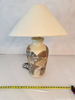 Front view of ceramic lamp with shade showing pattern and measuring tape for height reference