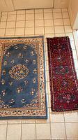 Blue area rug and red runner displayed side by side on tiled floor