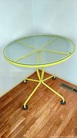 Full view of round patio table showing yellow metal frame and textured glass top