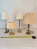 Group shot of four brass table lamps with shades, tape measure for scale