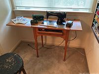 Singer Model 15-91 sewing machine in wood cabinet with pedal, manuals and attachments visible