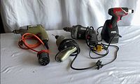 Group shot of Skil cordless drill on charger, three Black & Decker corded drills, hole saw attachment