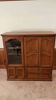 Front view of entire oak entertainment center showing glass door, paneled doors, drawers