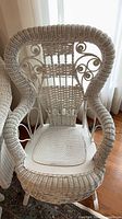 White wicker high-back armchair showing scrollwork and seat cushion