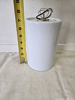 White cylindrical glass pendant shade beside measuring tape indicating ~6 in height