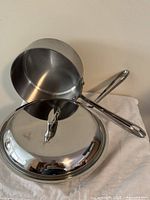 Side view showing one saucepan balanced on second pan; lid in foreground