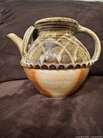 Front view of stoneware teapot showing dual handles, spout, scalloped band, glaze colors