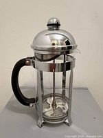 Full French press assembled showing stainless frame, glass carafe, black handle