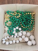 Top view of box containing green and gold bead strands and white graduated bead necklace