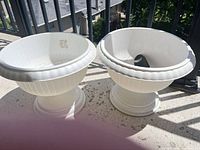 pair of white plastic pedestal urn planters on balcony