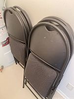 Two stacks of three folded metal chairs showing backrests with carry handles
