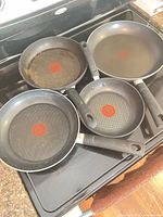Five T-fal frying pans displayed on stovetop, showing interiors and Thermo-Spot indicators