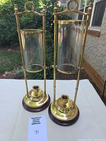 Front view of both polished brass hurricane candle holders with glass shades and wood bases