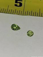 Pear and round peridot gemstones beside ruler for scale