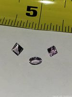 Three faceted light purple gemstones beside measuring tape showing size reference