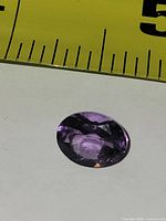 Oval faceted amethyst beside ruler showing roughly 10 mm length