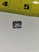 Top view showing rectangular step-cut light purple gemstone next to ruler for scale