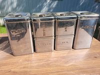 Group of four chrome canisters with lids showing size and labels