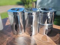 Front view of three chrome Kromex canisters showing labels and lids