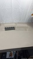Two clear plastic display cases side by side on table, left case contains black baseplate