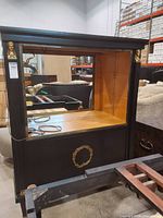 Front view showing black cabinet with open display area, gilded bust mounts and wreath ornament
