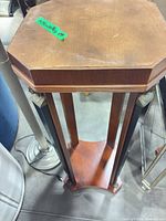 Full view of octagonal wood pedestal with lower shelf, showing finish wear