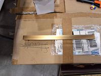 Long brushed brass rectangular cabinet pull handle on cardboard surface