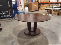 Full view of the round dark brown pedestal dining table in warehouse setting