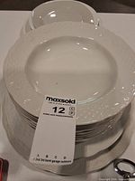 Stack of white porcelain dinner plates showing scalloped embossed rim, MaxSold tag indicating quantity 12