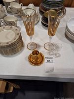 Two gilded champagne flutes, two cordial glasses, one gold-tone holder with plate on table