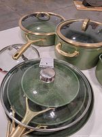Overall view of cookware set showing green finish, gold handles, glass lids, two fry pans and two pots