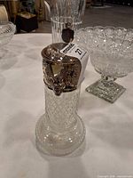 Full view of cut glass pitcher with ornate silver-plated lid featuring cherub design