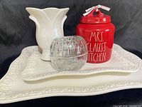 Group view of two white platters, white vase, red cookie jar, clear glass votive