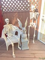 Two skeletons, gargoyle statue on pedestal, wicker chair on deck