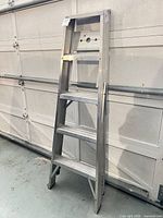 Full view of 6 ft aluminum 4-step ladder leaning against garage wall
