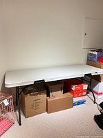 Full view of white plastic folding table set up against wall, boxes beneath not included