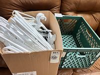 Box with numerous white plastic hangers next to a green plastic milk-style crate