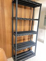 Full view of plastic shelving unit showing all five shelves assembled against wood panel wall