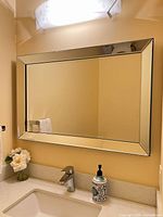 Front view of rectangular wall mirror mounted above sink, showing full reflective surface and mirrored frame