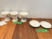 Group of three Wedgwood posy vases and two Royal Worcester plates displayed on wood surface