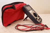 Multimeter standing with probes coiled and red carry bag