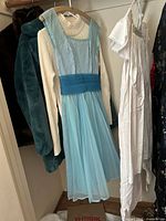 Group of garments including blue chiffon dress, cream sweater, teal coat, white cotton garment