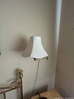Full view of one wall-mounted brass swing-arm sconce with white embroidered bell shade