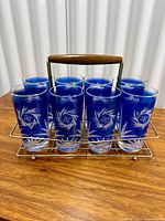 Eight blue cut-to-clear tumblers in metal carrier on wooden surface