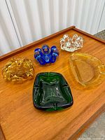 Five assorted art glass ashtrays on wooden surface